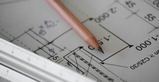 Projeto arquitetônico em planta baixa com lápis e régua sobre a mesa, representando o planejamento técnico necessário para a aprovação do alvará de construção.